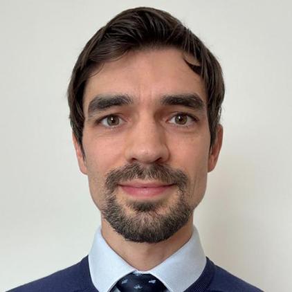 A white thirty-something male with short brown hair, wearing a blue jumper over shirt and tie. The type of person who looks like his name is probably ‘Matt’.