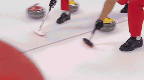 A curling stone heads rapidly across the ice towards some stationary stones. A ricochet knocks a competitor over onto the ice. Teammates rush in to help.